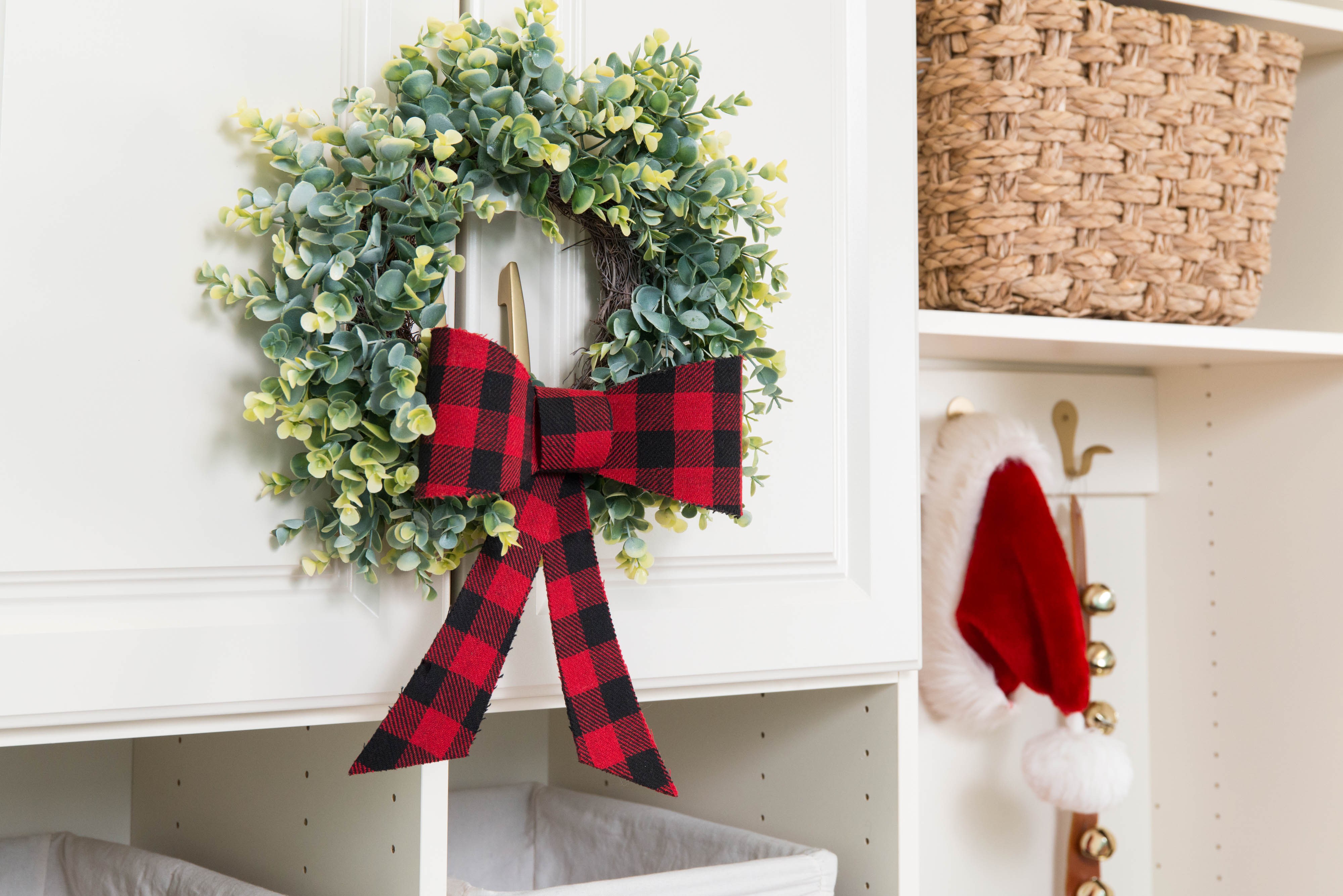 Christmas wreath on cabinet with Santa hat hung up and baskets. 