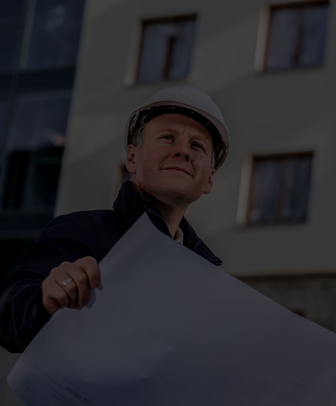 Male developer looking at plans. Dark gray overlay over image.